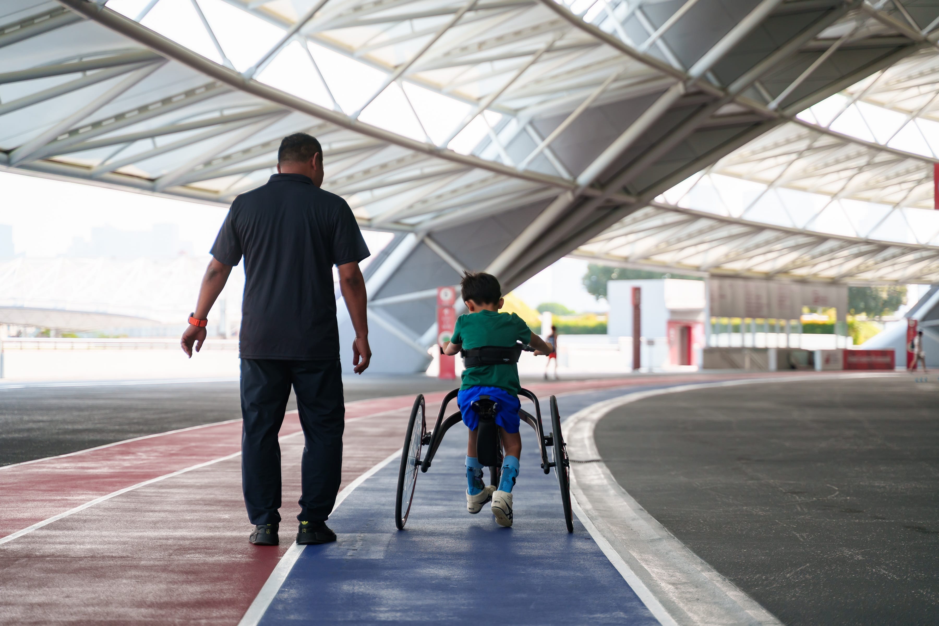 The backview of an older man walking alongside a young boy on his frame running equipment.
